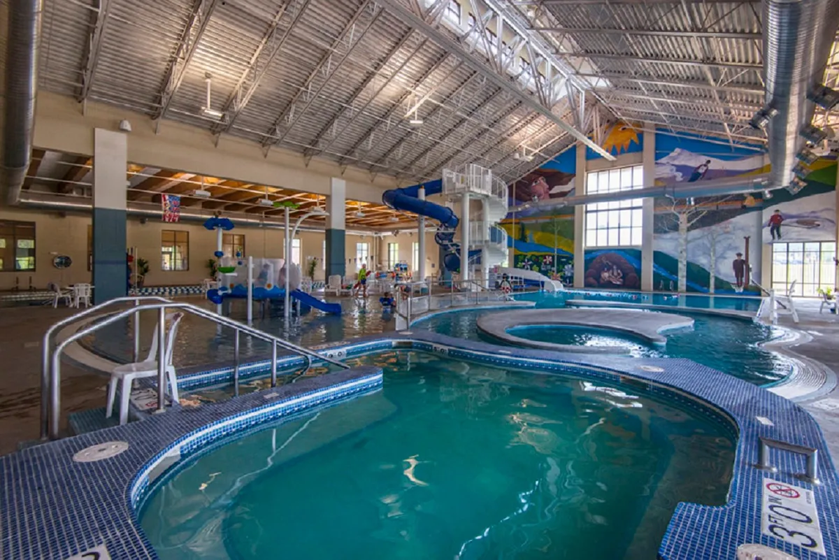 A vibrant indoor pool area with a colorful water slide, cheerful children playing, and comfortable seating for families. The energetic, family-friendly mood highlights a fun way to unwind after outdoor adventures.