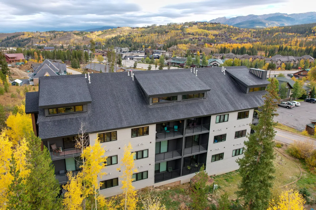 A modern building nestled among vibrant autumn foliage, with a distant mountain range forming the backdrop. The scene hints at hiking and biking opportunities right outside the property, while the overall mood is tranquil and rejuvenating, inviting exploration.