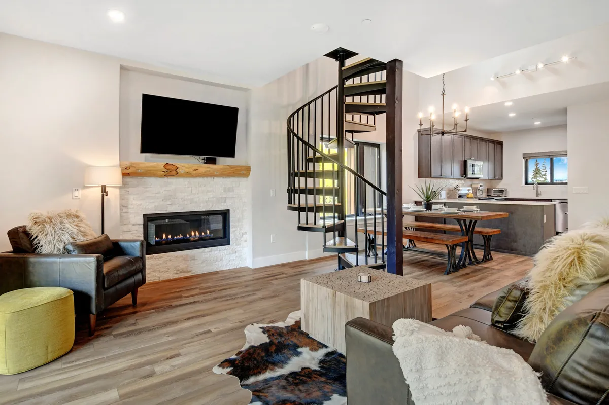 This inviting interior features a cozy fireplace surrounded by plush seating, a spacious dining table perfect for group meals, and a striking spiral staircase leading to the penthouse's upper level, all set in a warm and welcoming atmosphere.