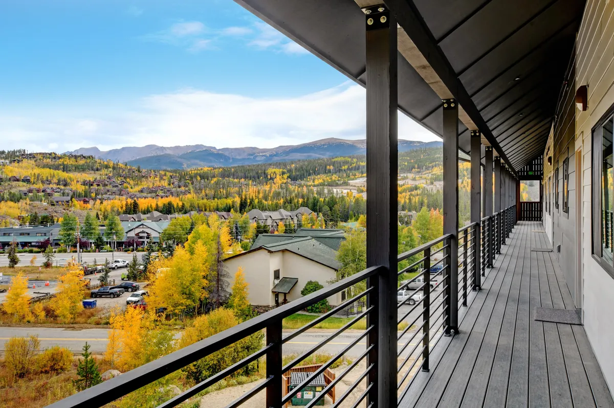 A serene balcony view overlooking a mountain range with fall foliage and neighboring buildings visible. The balcony railing is in the foreground, inviting guests to relax and enjoy breathtaking sunsets or watch local wildlife.